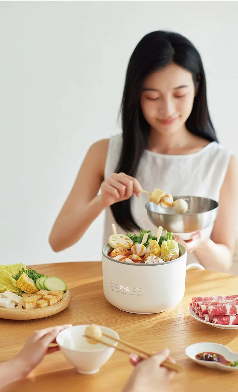 Smart white mini electric rice cooker on tabletop with person serving food