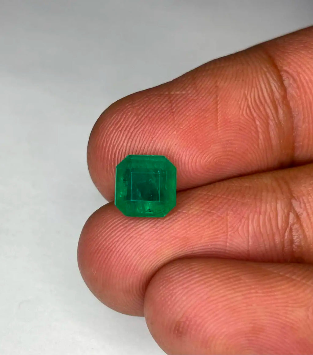 Green emerald gemstone, square octagon cut close-up held in fingers