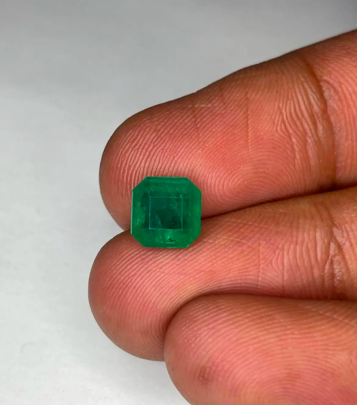 Green emerald gemstone, square octagon cut close-up held between fingers