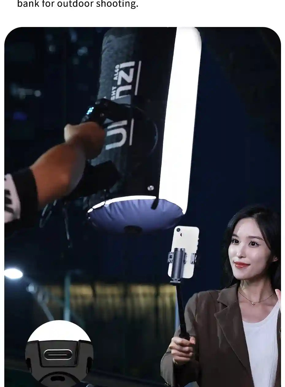 Portable LED light tube with black housing and bright panel, held by hand to illuminate a person filming with a phone.
