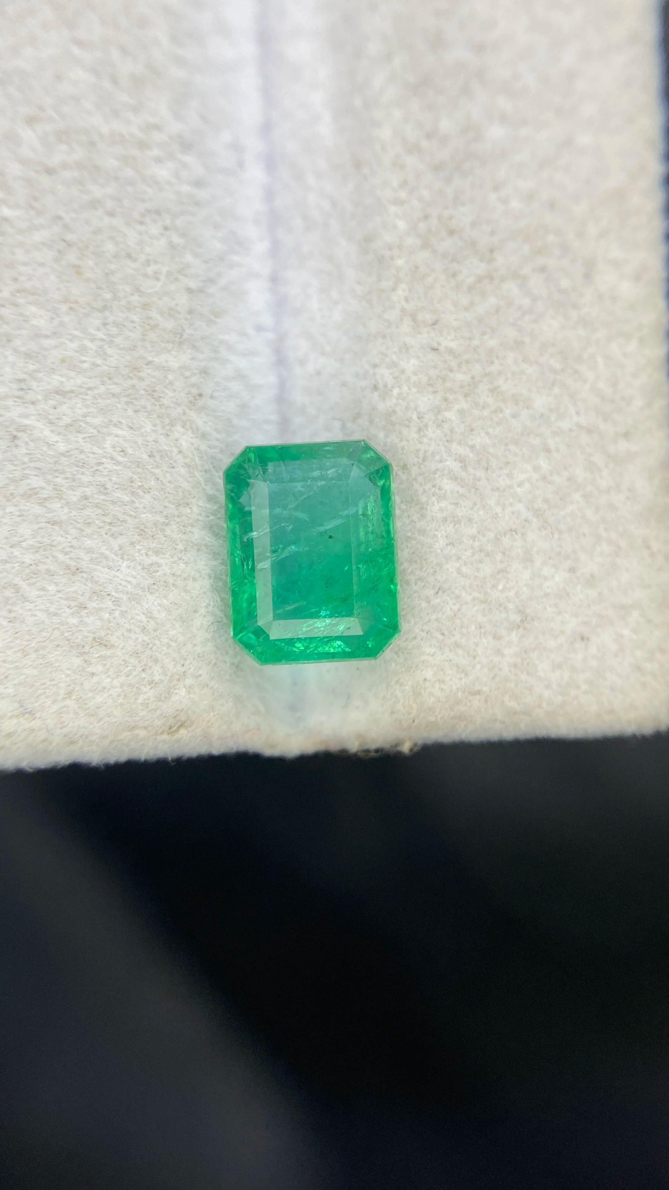 Green emerald-cut octagon gemstone close-up on white cloth, sharp step facets