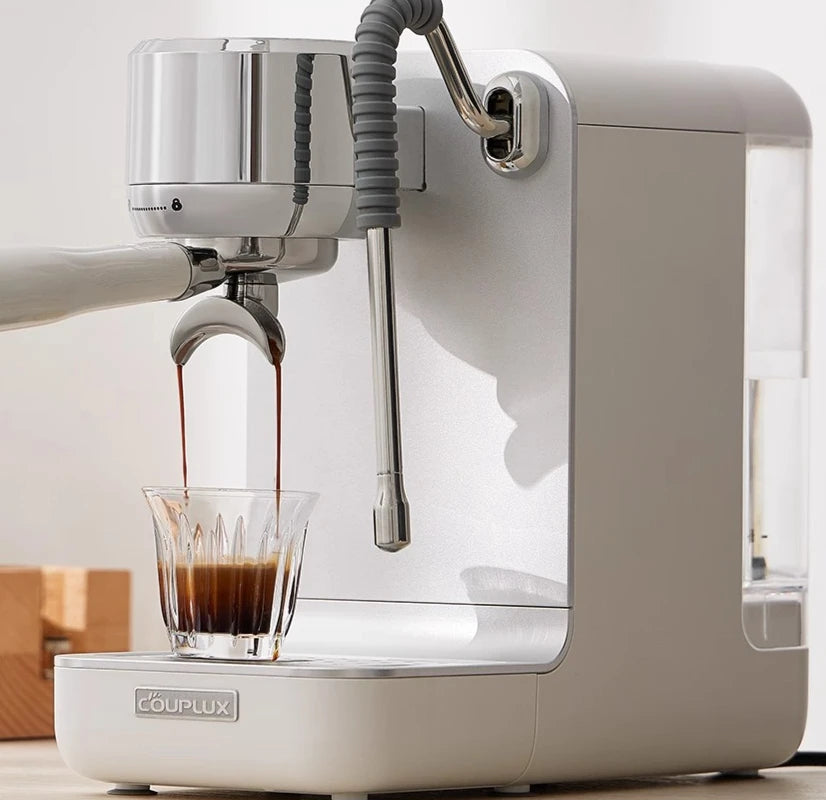 Couplux white espresso machine with chrome accents pouring a fresh shot of coffee into a crystal glass.