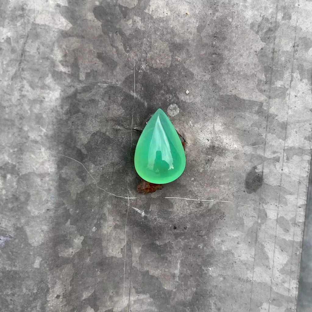 Green chrysoprase pear-shaped cabochon gemstone, polished teardrop on gray stone surface.