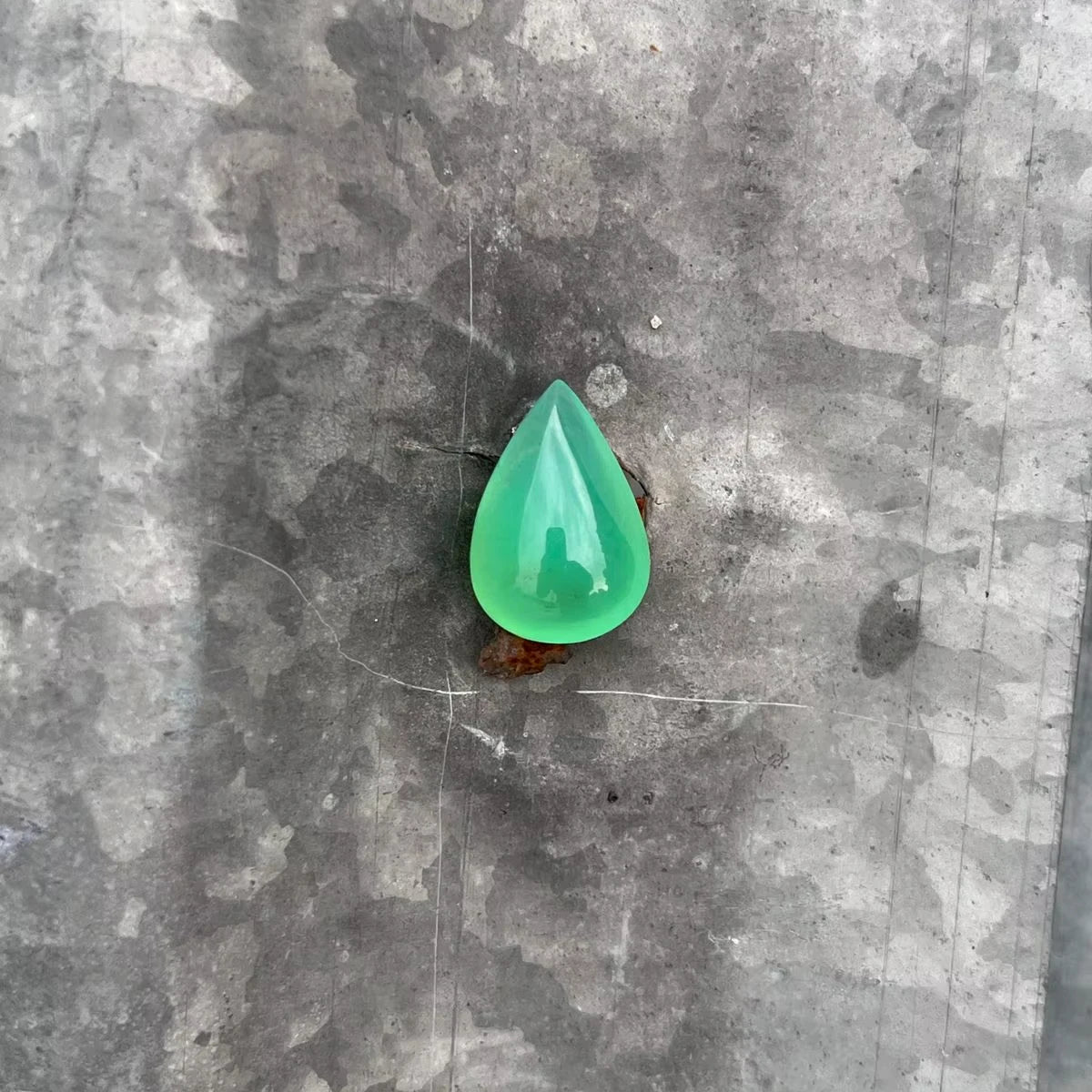 Green chrysoprase pear-shaped cabochon gemstone, polished teardrop on gray surface.