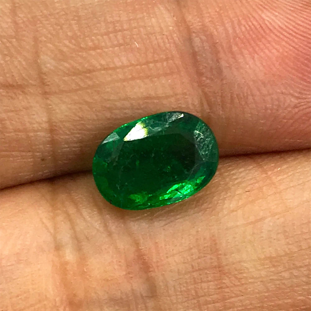 Green oval faceted loose gemstone on fingertip, glossy highlights
