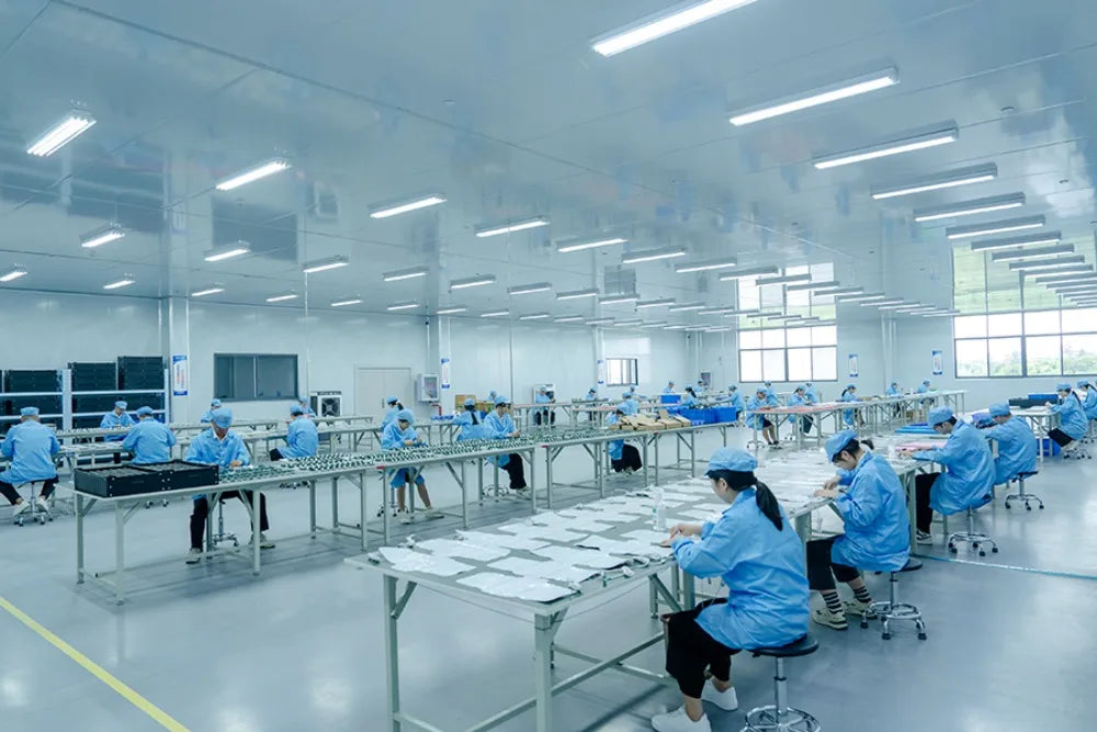 Workers in blue uniforms assembling Frovab rTMS brain stimulation machines for Parkinson's rehab in a clean factory.