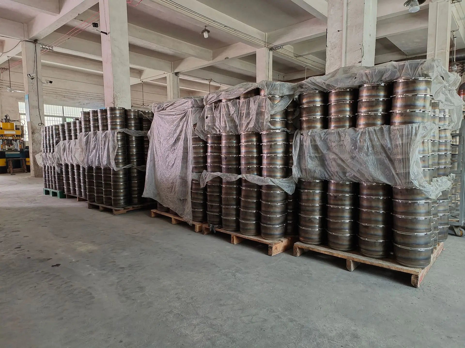 Stacked stainless steel pressure cooker parts and lids on pallets in warehouse