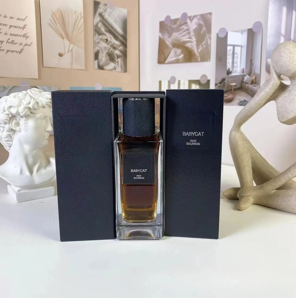 Babycat Raw Bourbon perfume in a rectangular glass bottle with a black cap, displayed inside a matching black box.