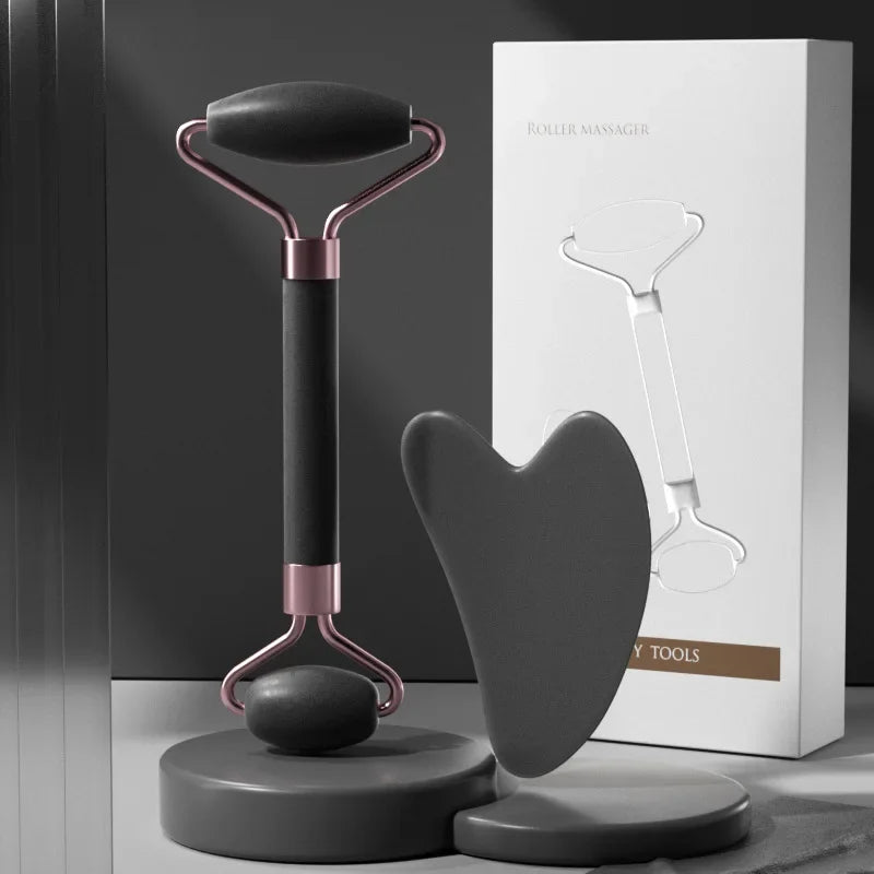 A dual-ended matte black face roller with rose gold accents and a heart-shaped gua sha board, shown with packaging.