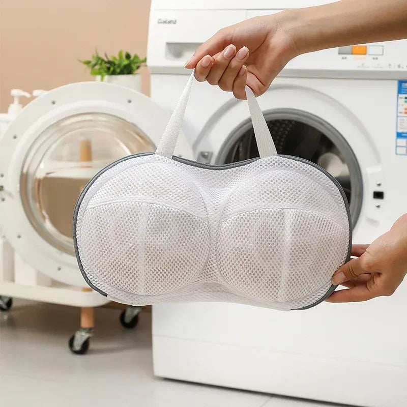 Bra washing bag held by handles in front of a washing machine to protect delicate lingerie during machine washing.