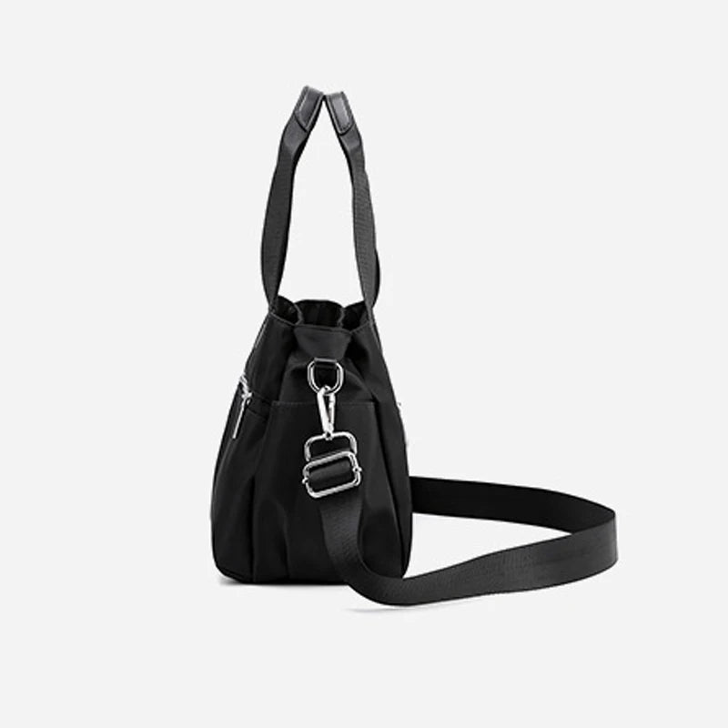Minimalist black canvas designer handbag with top handles, side pocket, and detachable adjustable shoulder strap.