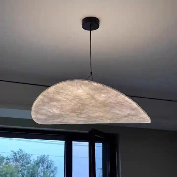 Crescent-shaped pendant light with a textured, off-white paper shade and a black ceiling mount for ambient lighting.