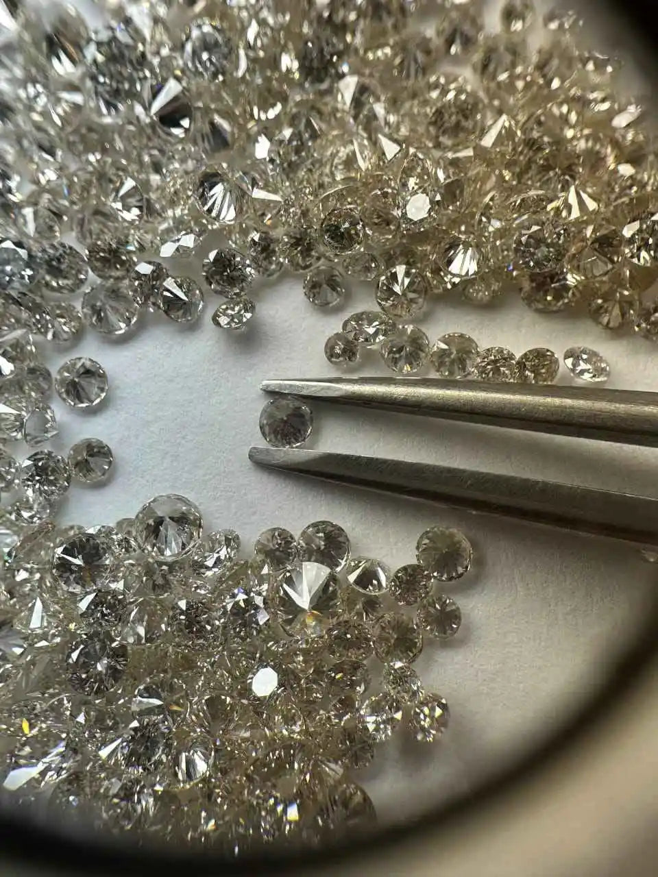 Loose round brilliant diamonds, white, close-up with metal tweezers and loose stones