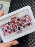 Mixed-color cushion-cut loose gemstones in white tray, red pink and purple tones