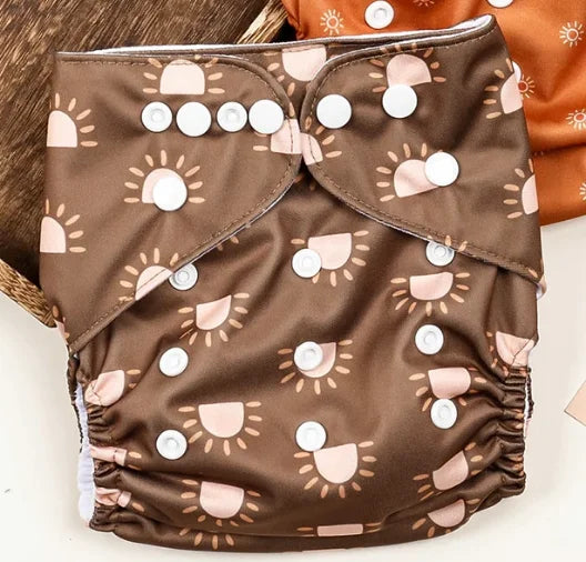 Reusable baby cloth diaper in brown with a cream sun print, featuring adjustable snap buttons for a perfect fit.