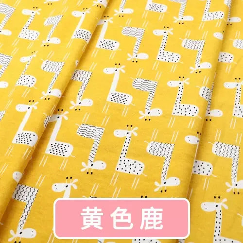 Yellow knit fabric featuring a repeating black and white giraffe print pattern, ideal for children's clothing.