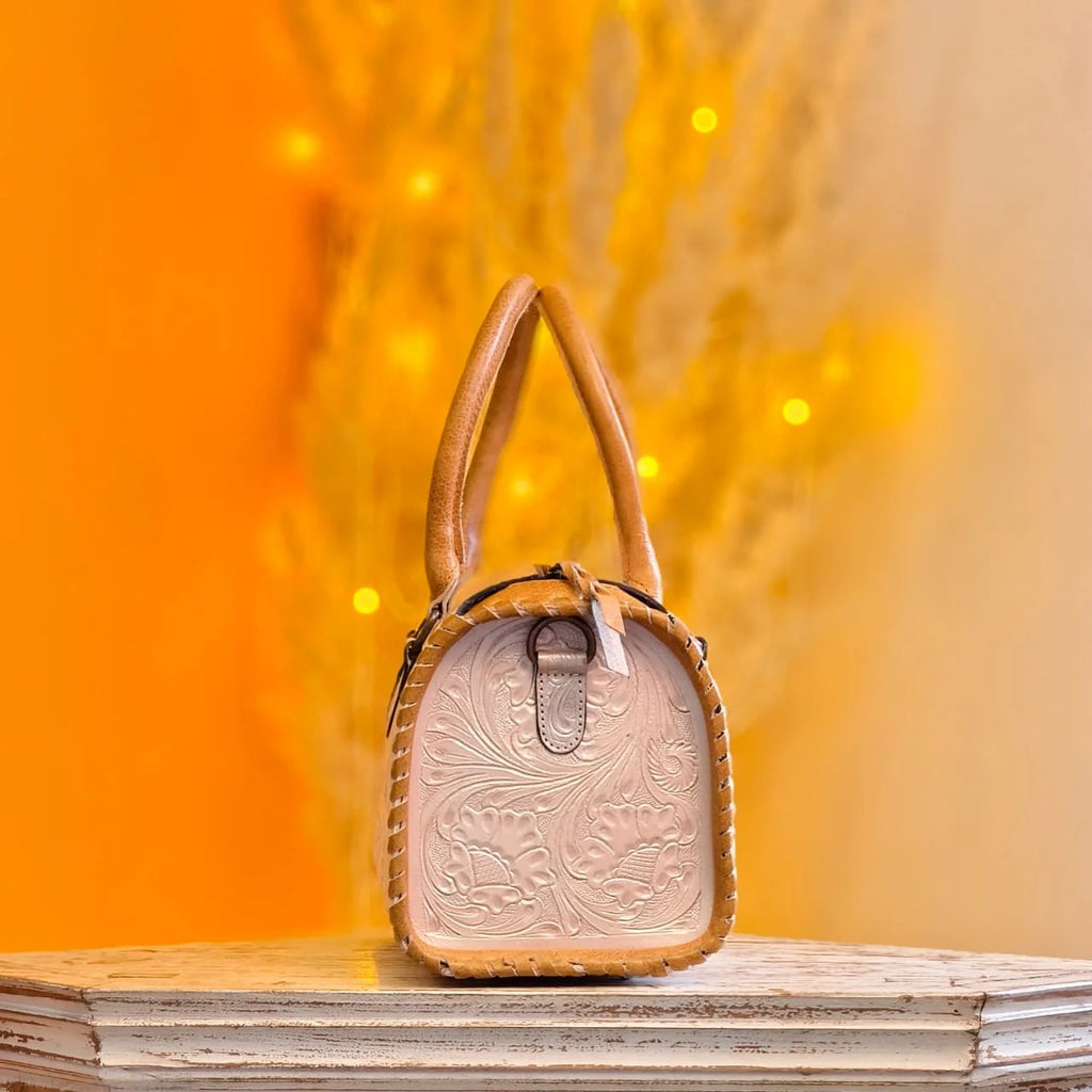 Tan genuine leather mini duffel bag with hand-tooled floral carvings and whipstitched edges, designer handbag style.