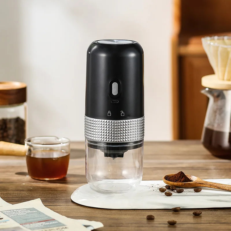 Black portable electric coffee grinder with silver textured grip and clear container on wooden table.