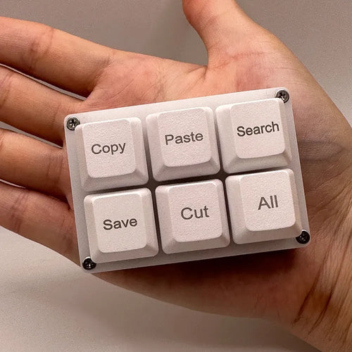 White, 6-key programmable mechanical macro keypad with custom shortcut labels held in a palm.