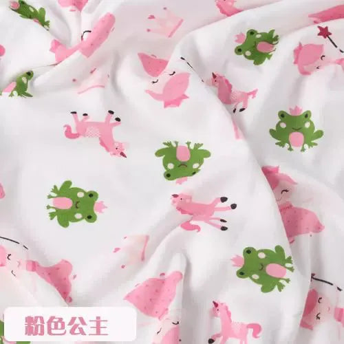 Tidesmit white knit jersey fabric featuring a pattern of green frogs, pink princesses, and unicorns for baby clothing.