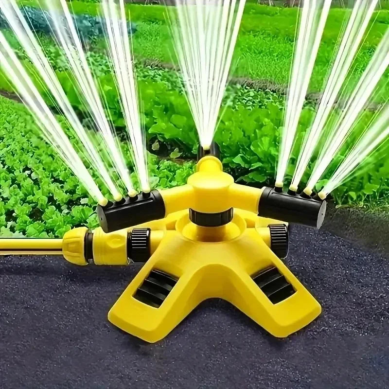 Yellow and black rotating lawn sprinkler spraying fine jets over green garden beds