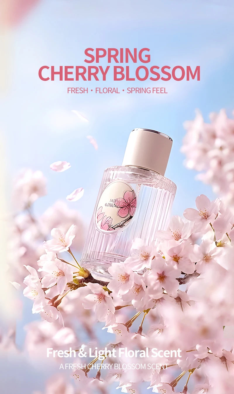 Clear glass perfume bottle with a sakura label, surrounded by delicate pink cherry blossoms against a blue sky.