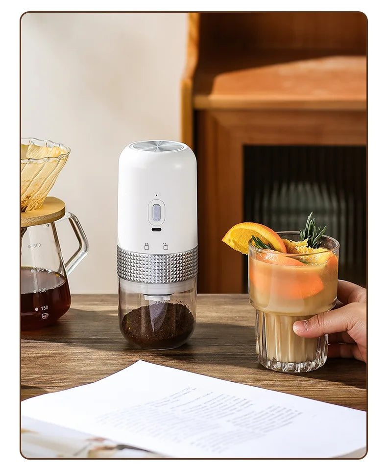 Portable white electric coffee grinder with metallic textured grip and clear container on wooden table.