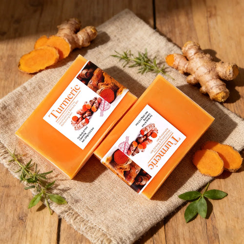Two orange 100g anti-inflammatory turmeric soap bars with raw turmeric roots on a burlap background.