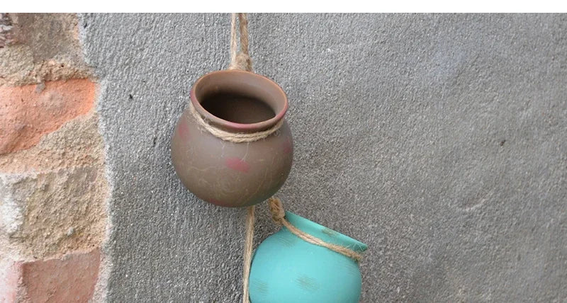 Ceramic hanging flowerpots on a wall: small beige pot and teal pot with rope
