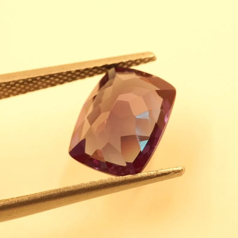 Cushion-cut alexandrite gemstone with facets, dark reddish-brown, held on gold-toned supports