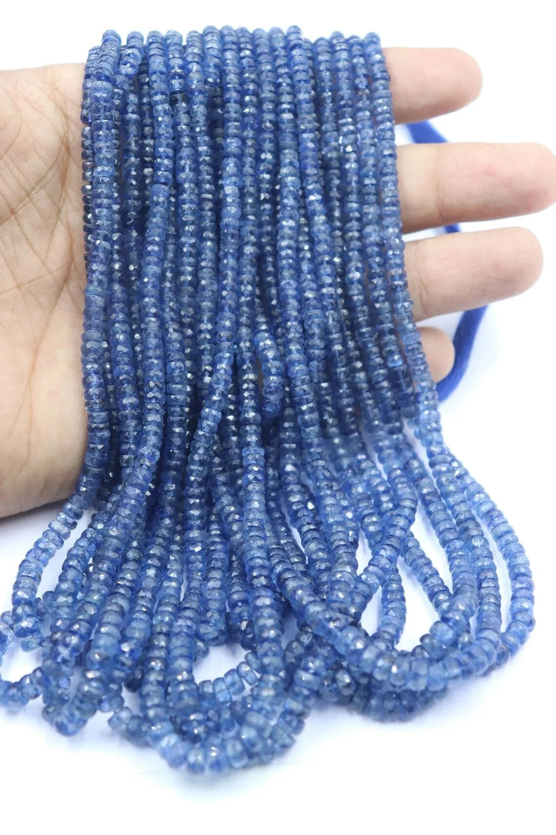 Kyanite rondelle bead strand held in hand, faceted blue beads with small drilled holes