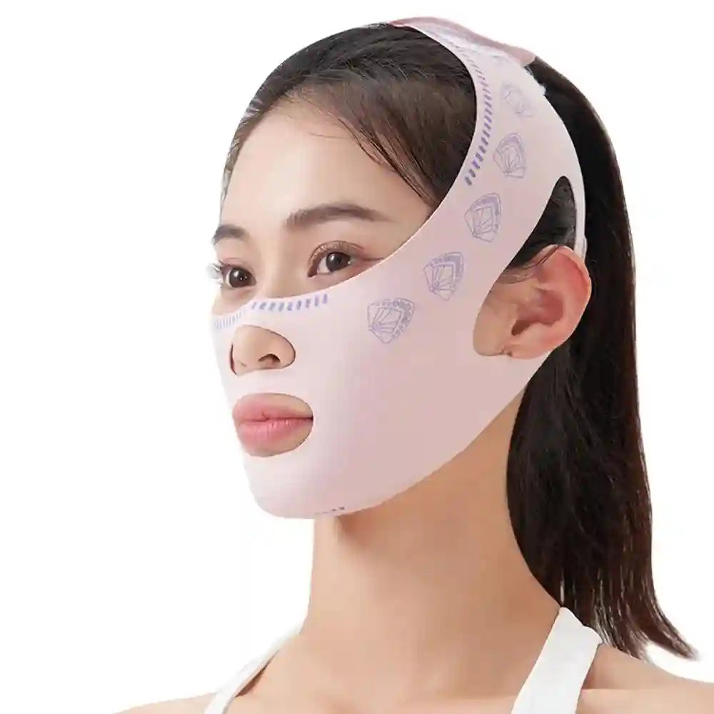 A woman wears a light pink, fabric V-line lifting face mask with a purple fan pattern, securing over her chin and ears.