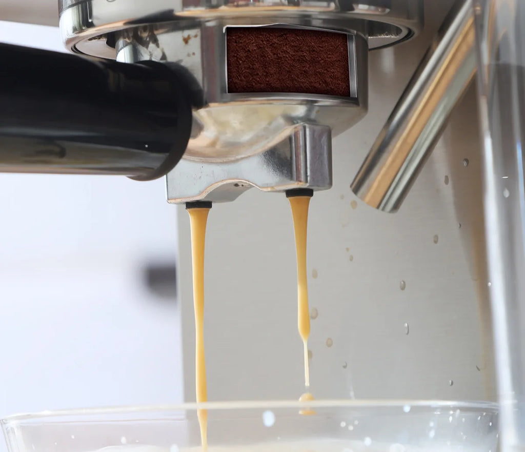 Stainless steel espresso machine pulling double shots of espresso through a portafilter into a glass cup.