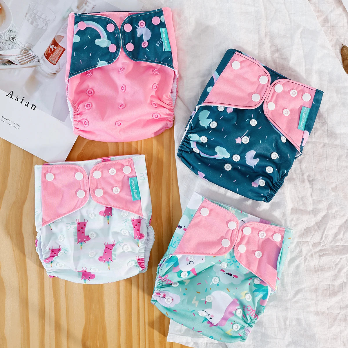 Four Happy Flute reusable baby cloth diapers with pink and unicorn prints on a white cloth background.