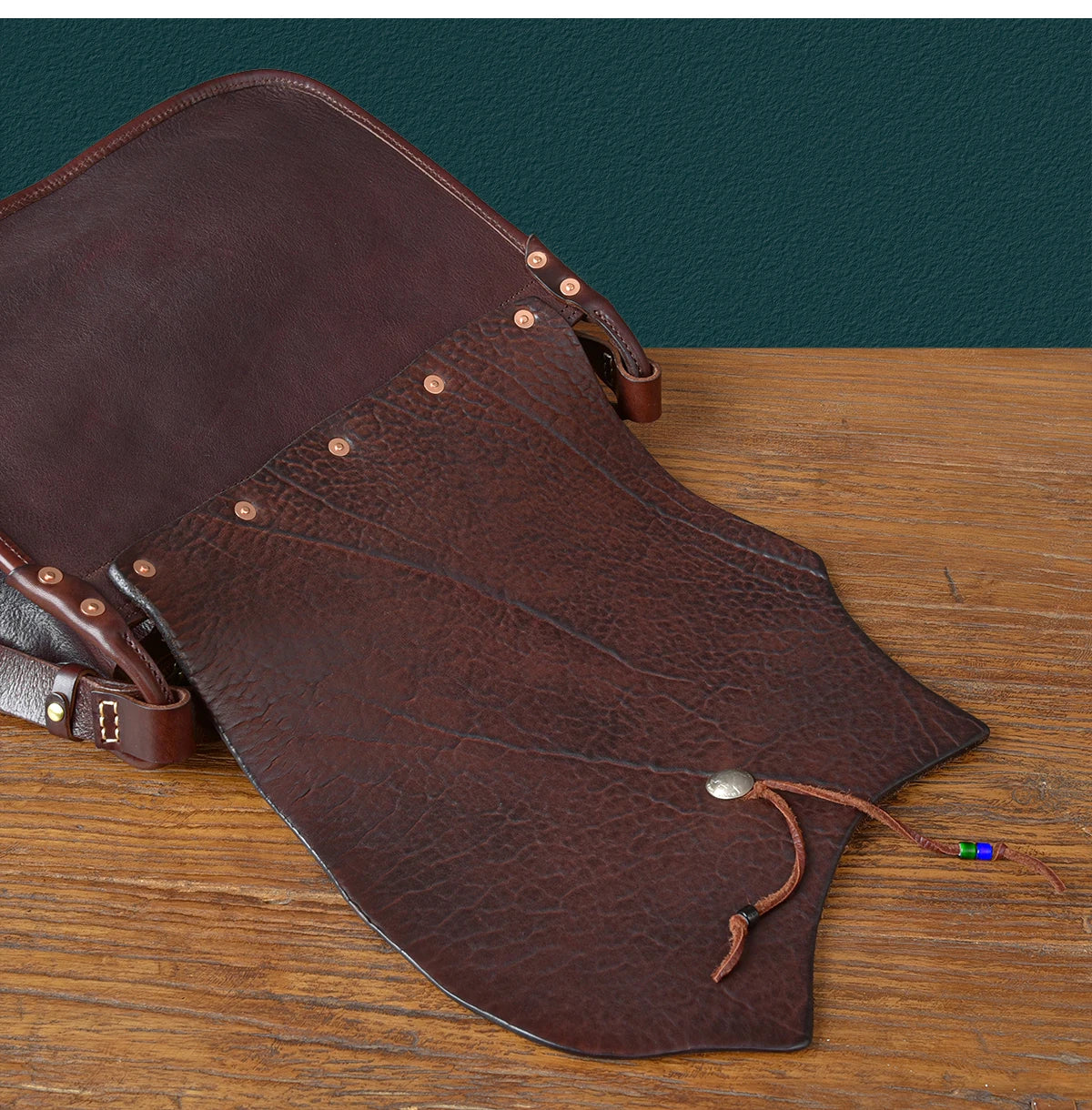 PNDME vintage dark brown genuine cowhide messenger bag with textured flap, copper rivets, and beaded leather tie.