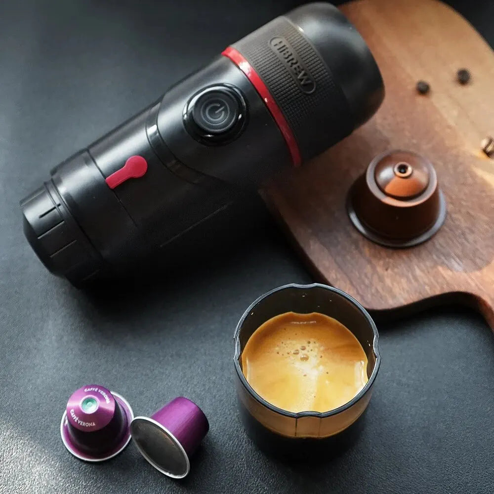 HiBREW portable black espresso coffee maker with red accents, capsule holder, and cup of fresh coffee on table.