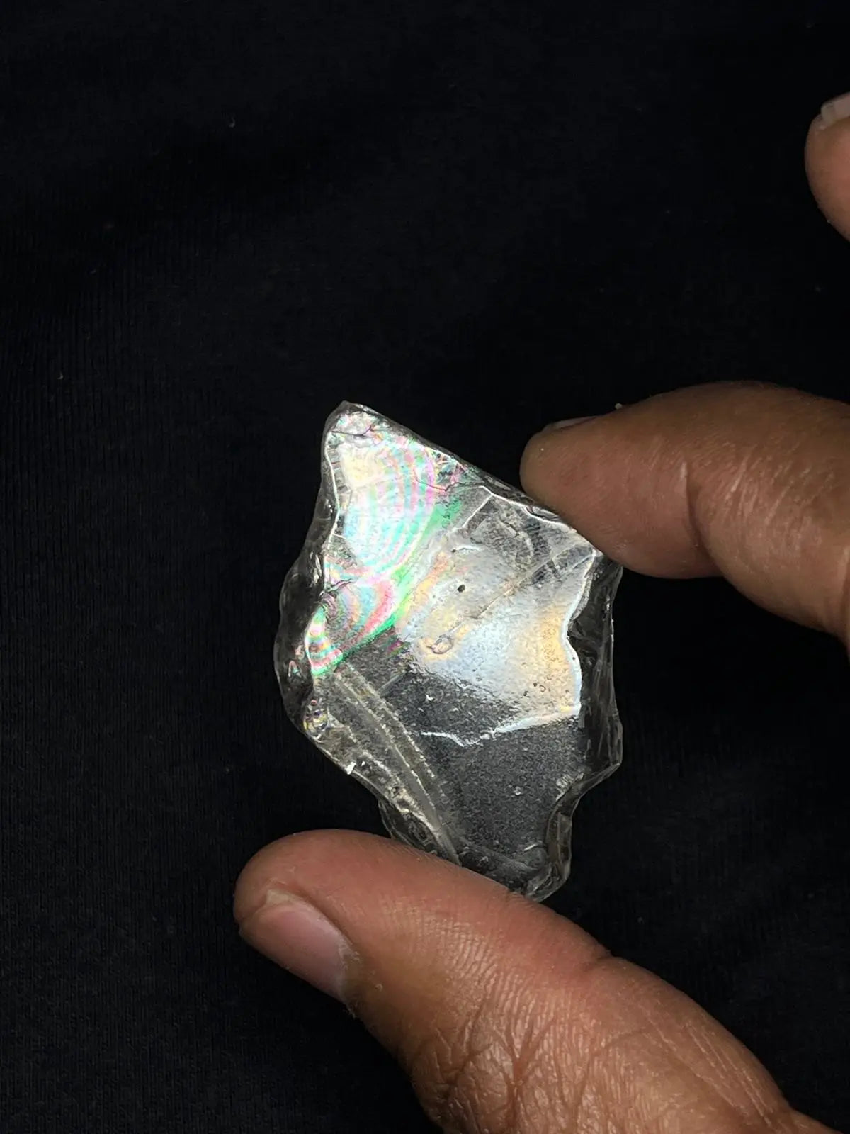 Hand holding dark polished rough gemstone, iridescent rainbow facets
