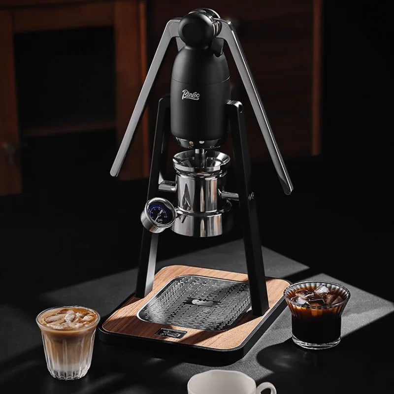 Binco manual espresso maker with black frame, chrome piston, pressure gauge, and wooden base on a black tabletop.