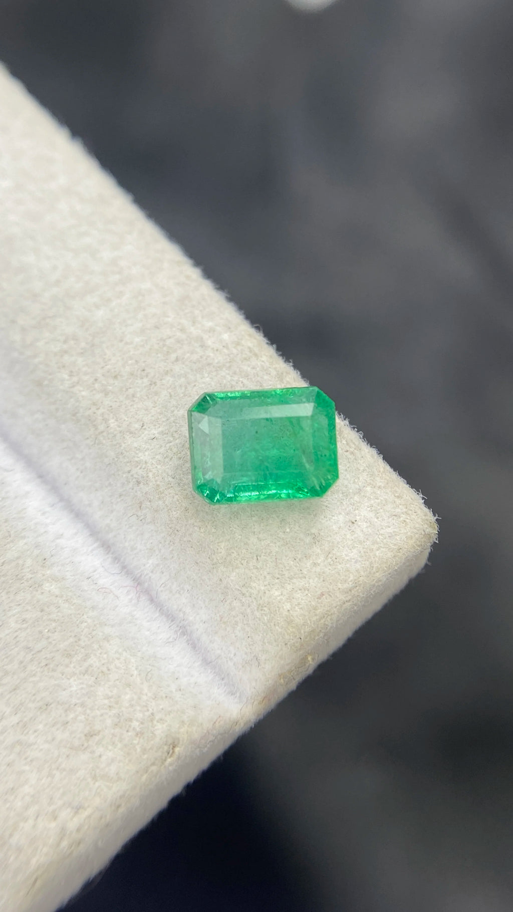 Green emerald-cut octagon gemstone close-up on white cloth, light reflection on top