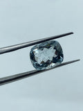 Sky-blue cushion-cut gemstone between metal tweezers, faceted