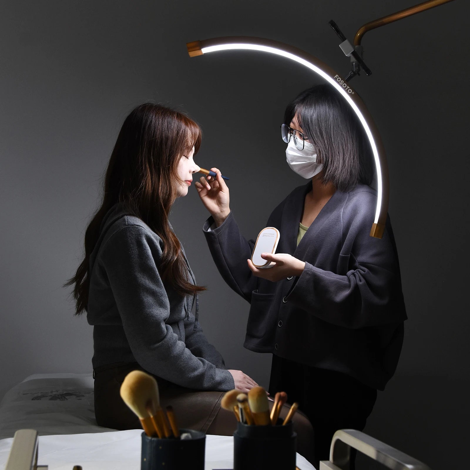 Curved LED beauty lamp providing bright, focused lighting for a makeup artist applying cosmetics to a client.