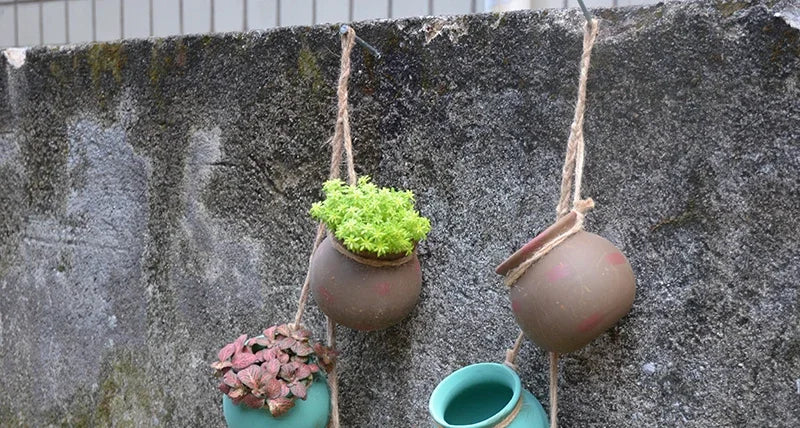 Set of four hanging ceramic planters with succulents on a stone wall