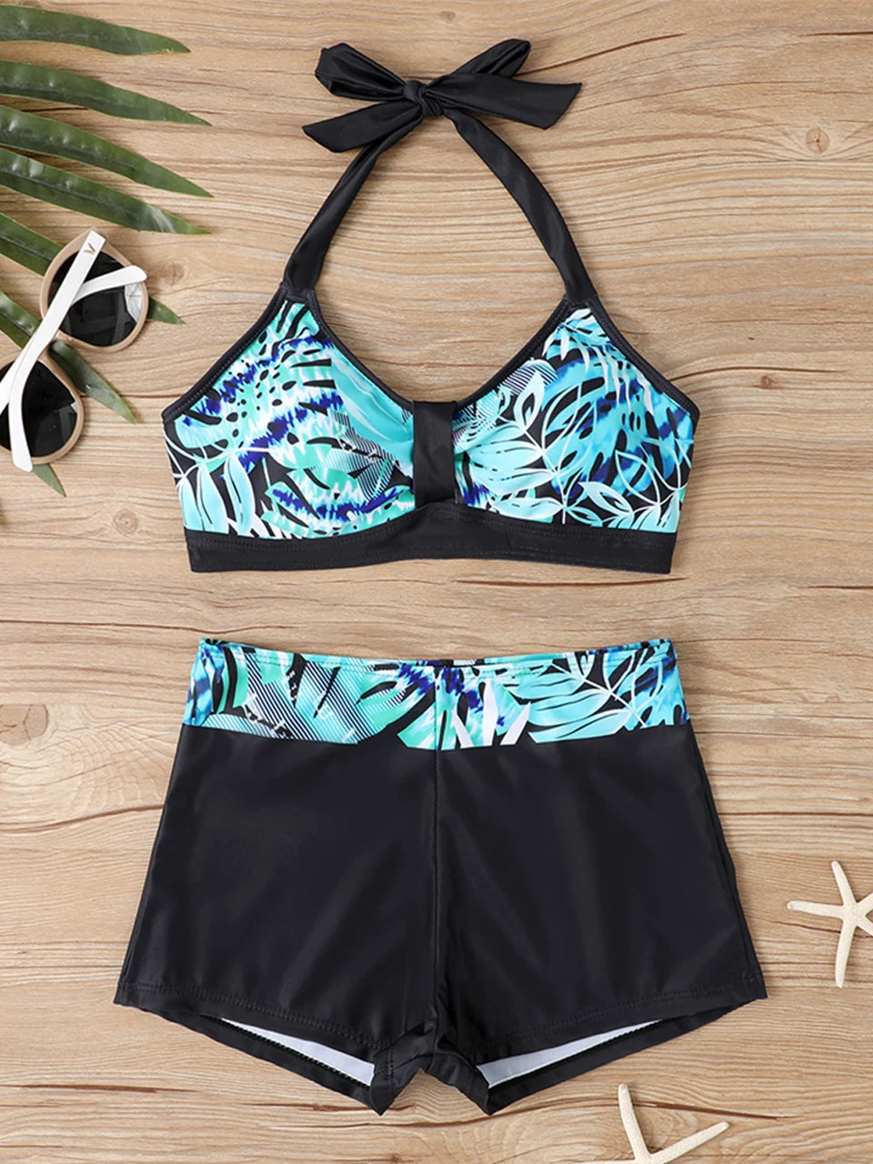 Tidesmit high-waisted bikini with blue and black tropical leaf print top and solid black high-cut shorts.