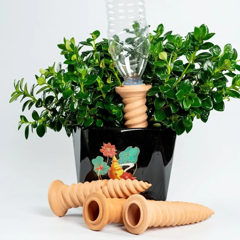 Terracotta self-watering stakes with clear reservoirs in a planter of green plants