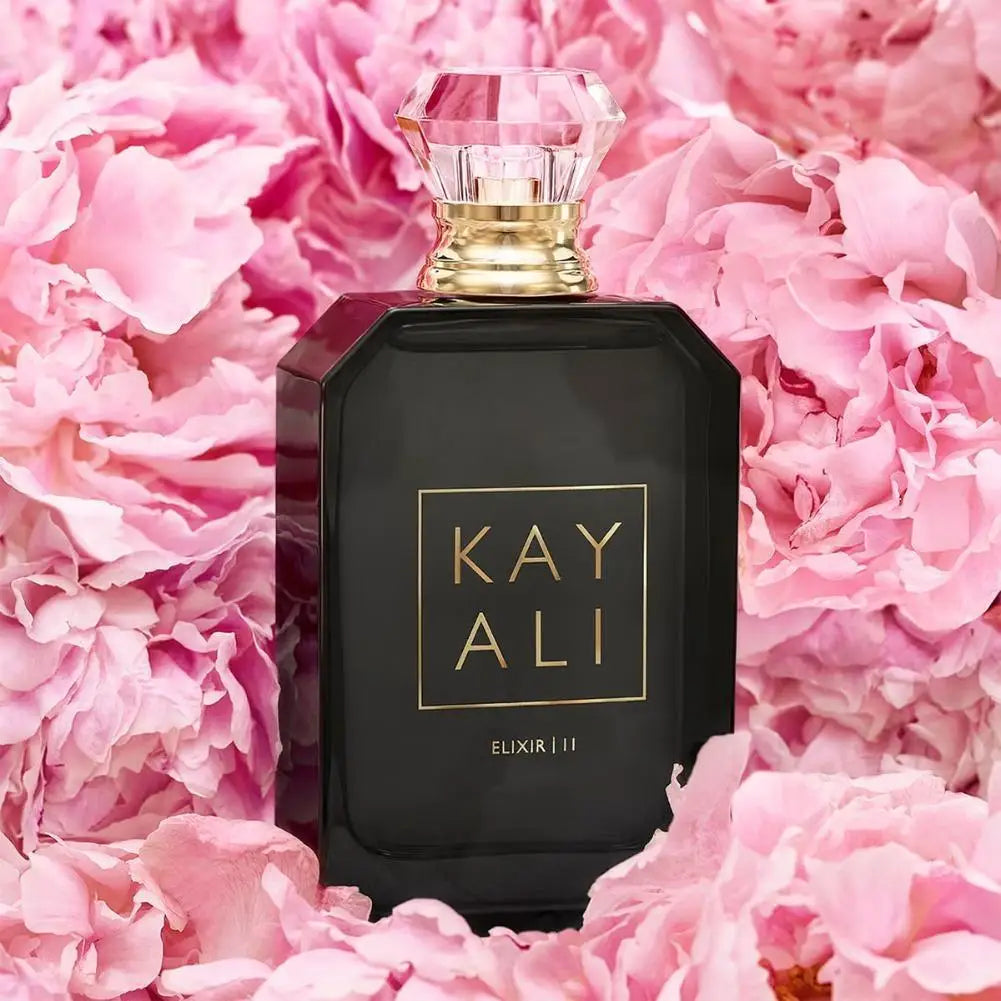 Kayali Elixir | 11 perfume in a rectangular black glass bottle with a faceted crystal cap, set amidst pink peonies.