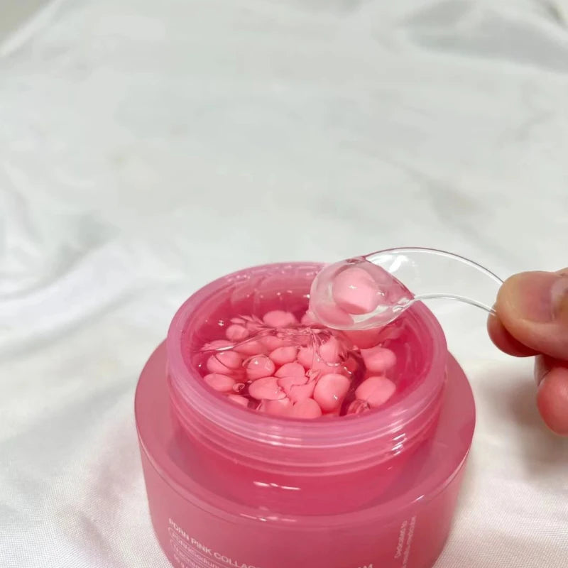 Pink jar of collagen capsule face cream with a clear spatula lifting a pink capsule from the clear gel base.