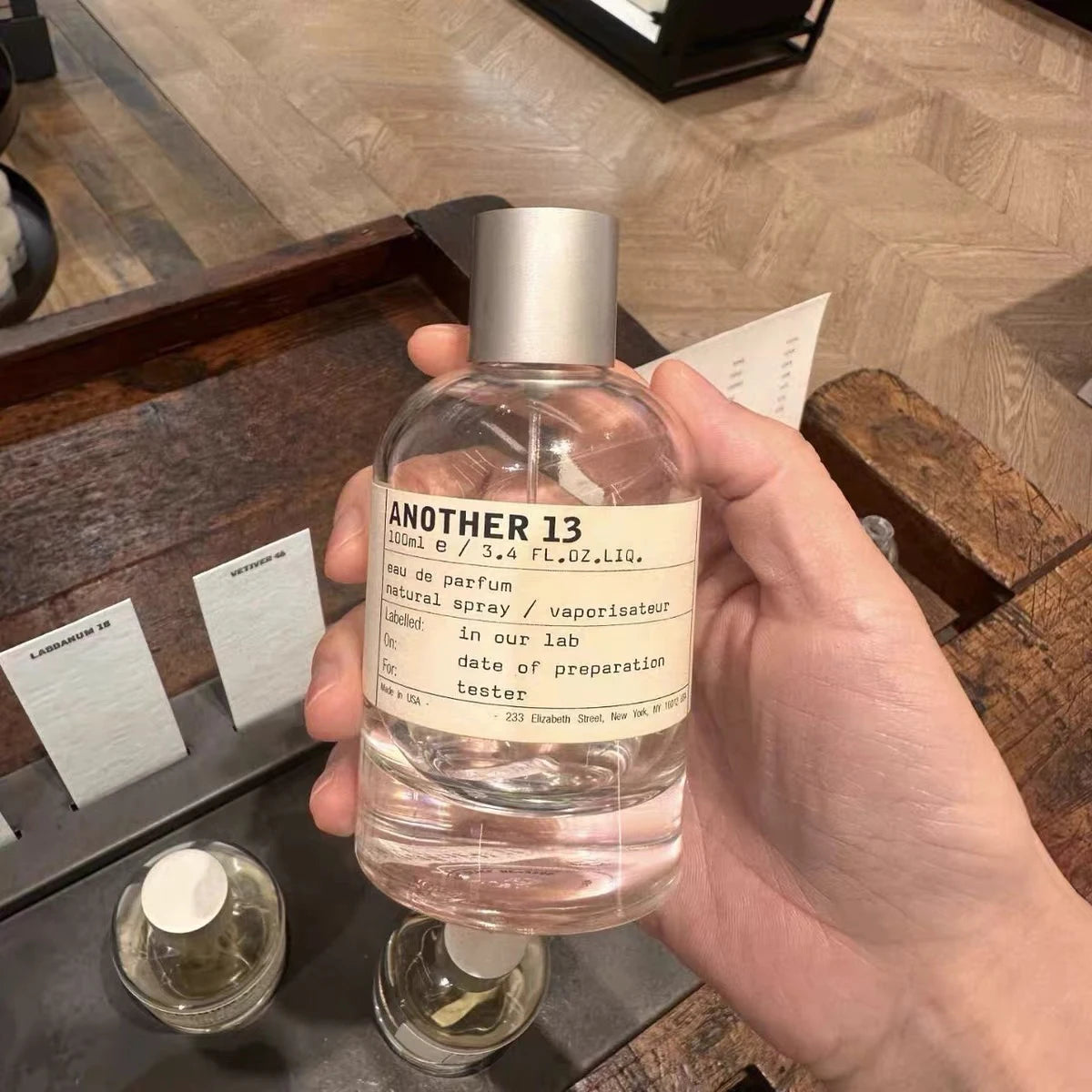 Another 13 eau de parfum in a 100ml clear glass spray bottle with a silver cap, held in hand.