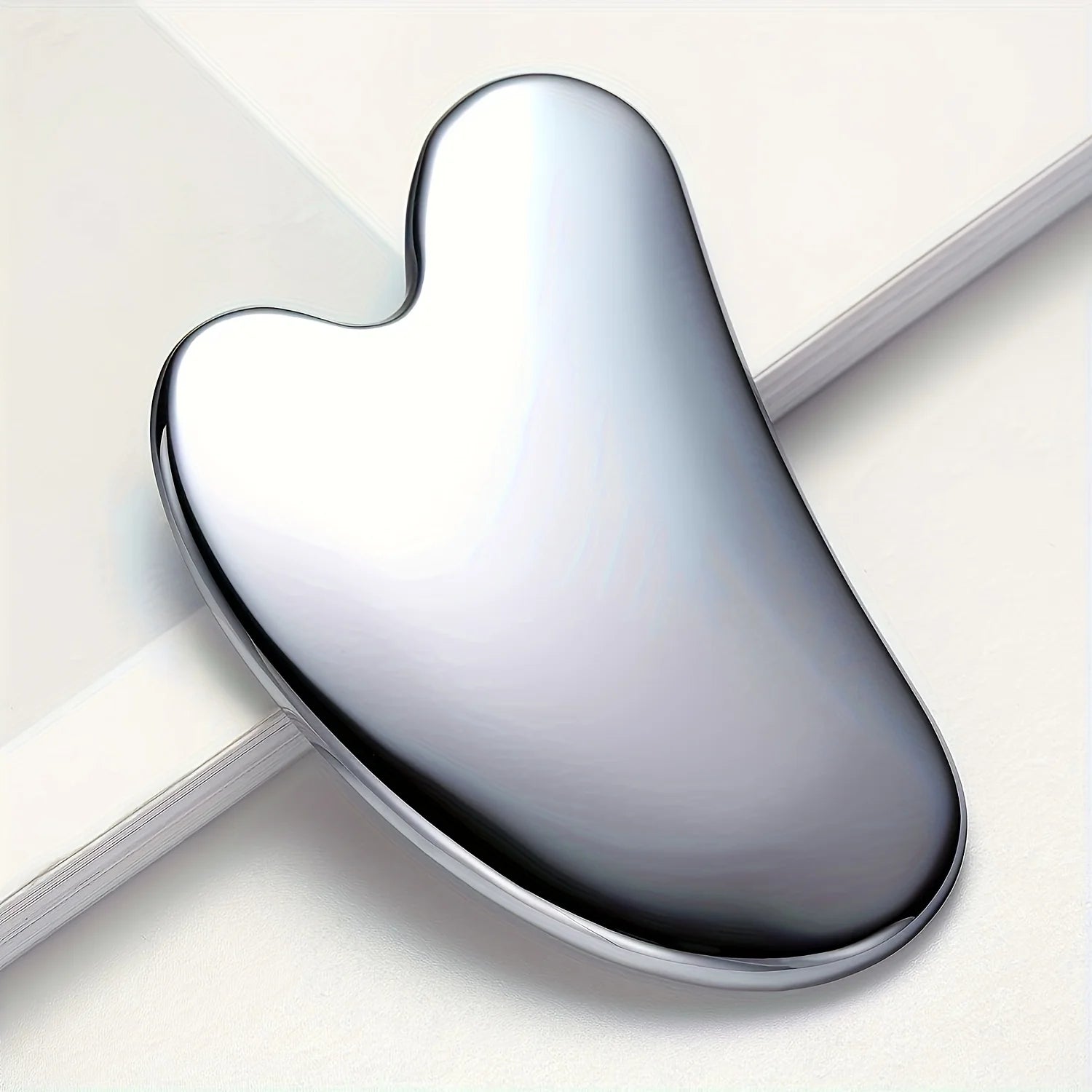 Smooth, silver stainless steel dolphin-shaped gua sha facial massage tool resting on a white surface.