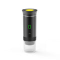Portable black electric espresso maker with yellow top button, green LED power light, and clear bottom cup.