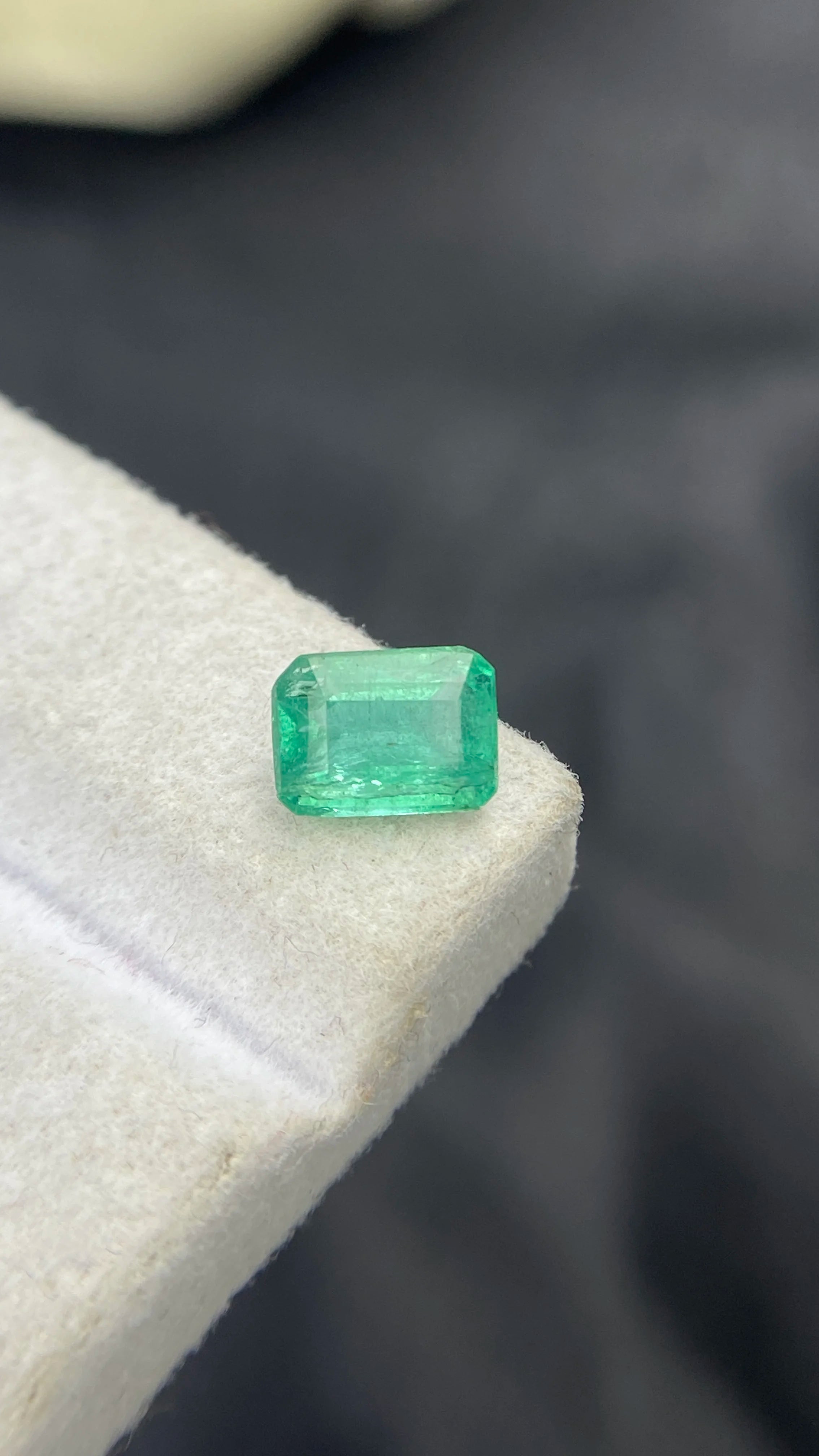 Loose emerald-cut green gemstone, angled view, on white felt pad
